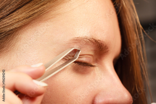 Woman tweezing eyebrows depilating with tweezers © Voyagerix