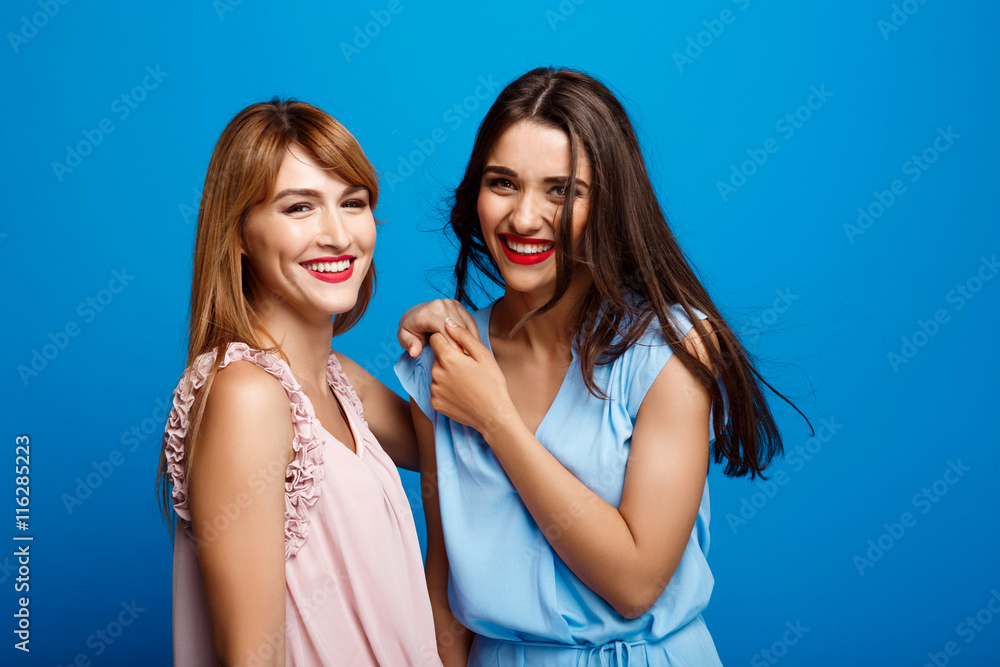 Portrait of two beautiful girls over blue background. Portrait of two beautiful girls over blue background.