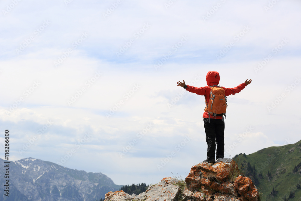 Obraz premium cheering successful woman backpacker open arms on mountain peak