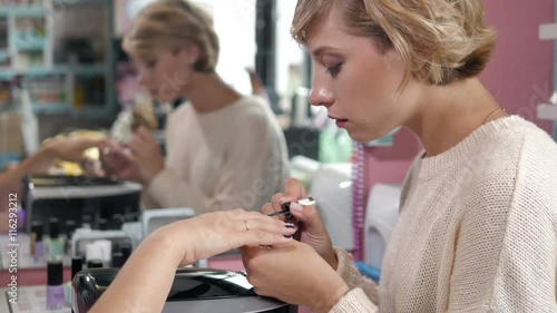 woman in a nail salon receiving a manicure by a beautician with nail file. Woman getting nail manicure. Beautician file nails to a customer. Blurred background photo