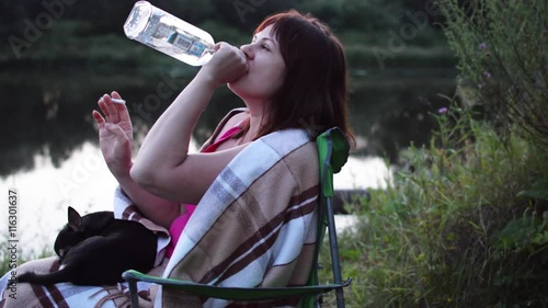 Girl on the Riverbank Drinking Alcohol Out of the Bottle and Smoking a Cigarette