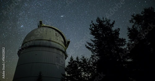 Rozhen astronomical observatory under the night sky stars. Blue sky with hundreds of stars of the Milky way. Observatory in a pine trees forest in the mountain. Moon light. Vignetting. Zoom tilt 4k.