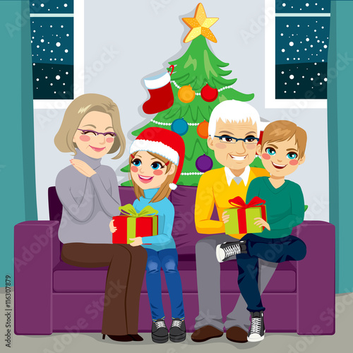 Grandparents with granddaughter and grandson sharing gifts in Christmas day sitting on sofa at home with tree on background