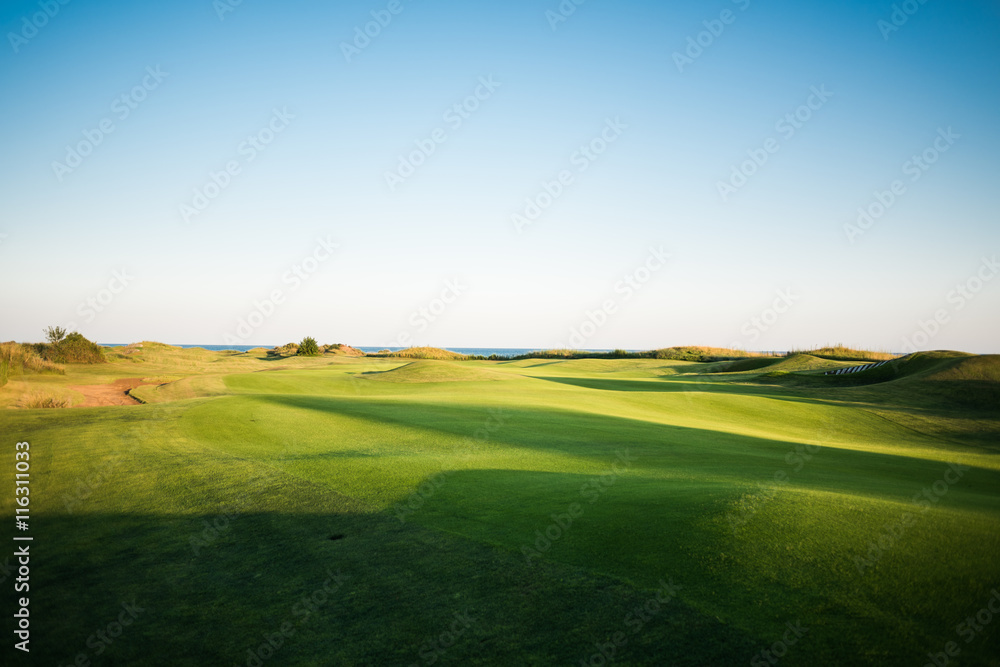 Beautiful golf course with sand traps and sea in the background at sunset
