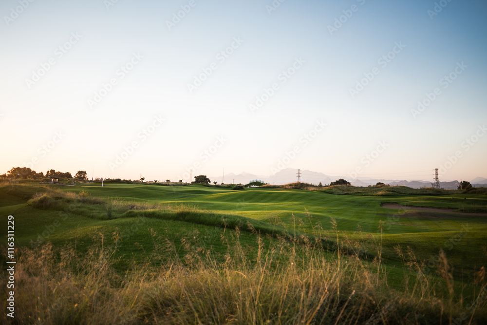 Beautiful golf course with sand trap and striped grass at sunset