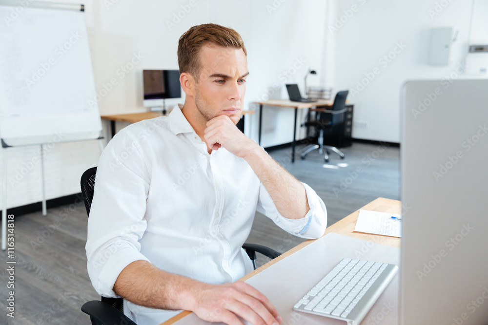 Fototapeta premium Thoughtful young businessman using computer at work
