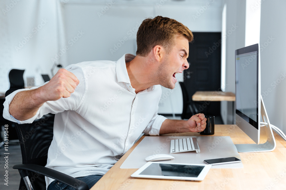 Aggressive furious businessman shouting and working with computer in office Aggressive furious businessman shouting and working with computer in office