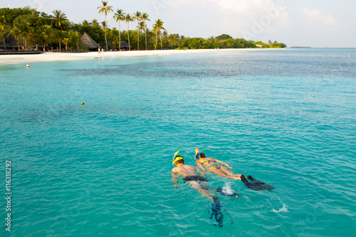 Caucasian couple of tourists snorkel in crystal turquoise water near Maldives Island