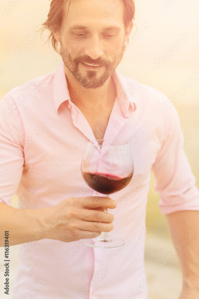 Confident and happy sommelier. Toned image of bearded mature man in pink shirt tasting red wine and looking at glass isolated on sea. Confident and happy sommelier. Toned image of bearded mature man in pink shirt tasting red wine and looking at glass isolated on sea.