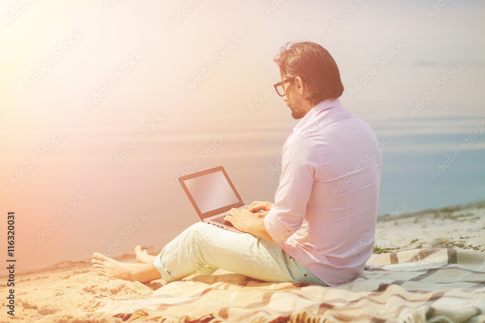 Toned picture of middle-aged poet working on his laptop computer. Handsome businessman in glasses making diagrams for new projects in evening near by sea.