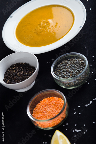 Cream soup of assorted lentil. Yellow and green lens, spices as raw for meal and lemon on black background. Healthy, appetizing, delicious, vegetarian food. Top view, copy space. 