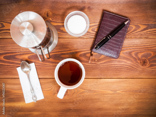 Tea set for breakfast on the table. Notebook with pen. View from above