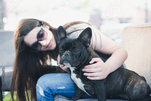 Beautiful young girl enjoying in a cafe bar with her French bulldog pet.