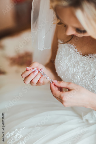 Unrecognizable bride in white dress holding beautiful earrings in hands.