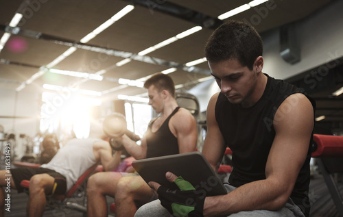 group of men with tablet pc and dumbbells in gym