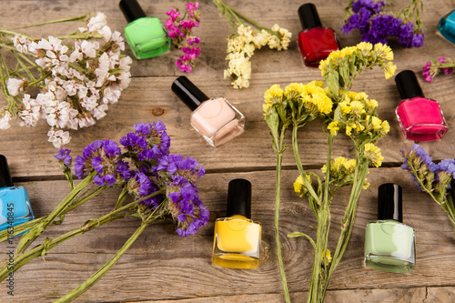 Bottles of colorful nail polish and flowers on brown wooden table photo