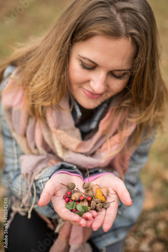 Girl walking in autumn park. Girl dressed in a coat and scarf. woman s hand  berries and acorns oak.