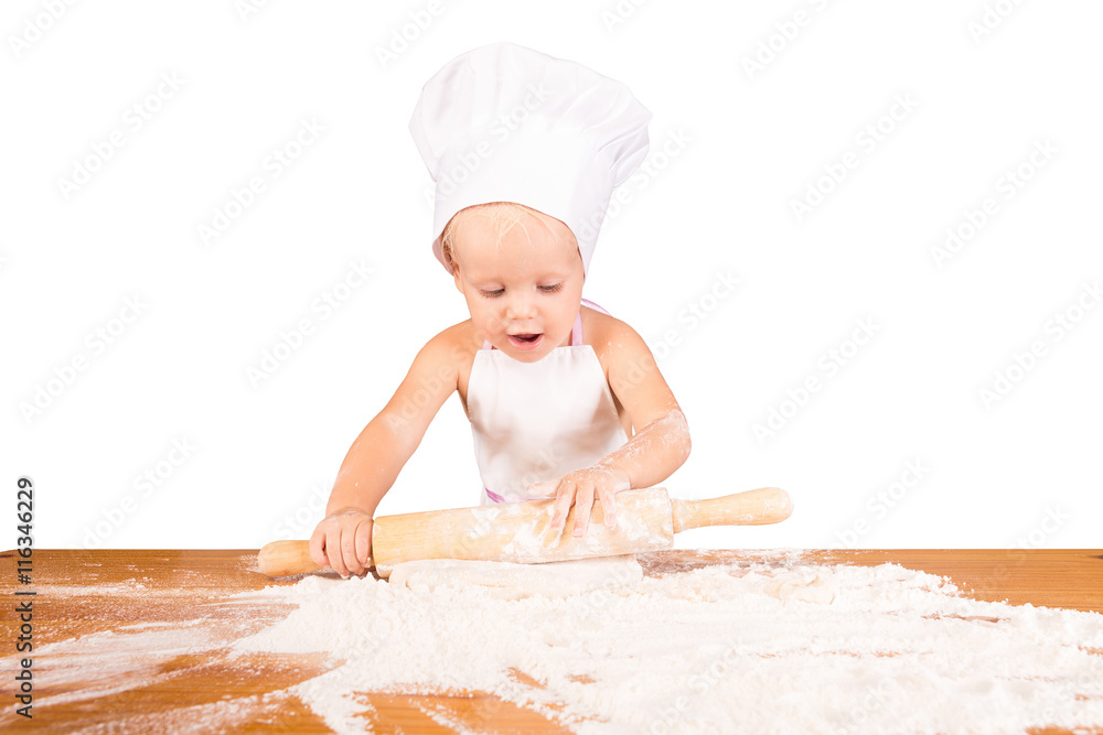 Small very beautiful baby in chef hat with pleasure unrolls dough of flour Small very beautiful baby in chef hat with pleasure unrolls dough of flour