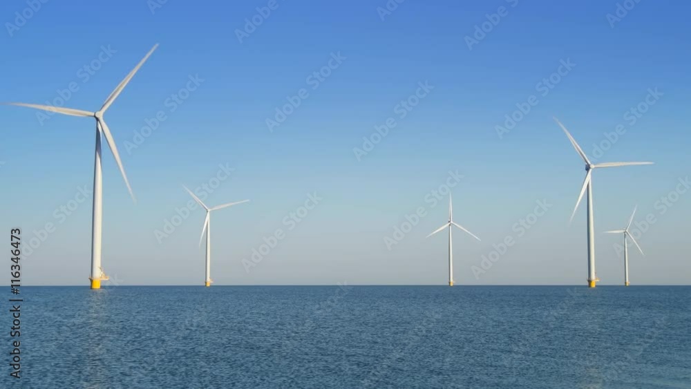 Wind turbines with rotating blades in an offshore wind park during a beautiful summer day. Wind turbines with rotating blades in an offshore wind park during a beautiful summer day.