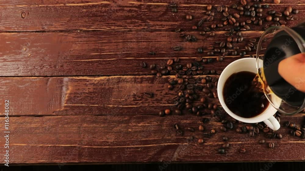 Pouring coffee into white cup and coffee beans on brown wooden table Pouring coffee into white cup and coffee beans on brown wooden table