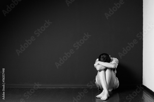  Sad woman sitting in the corner of a room, head on the knees, face is hidden, black and white