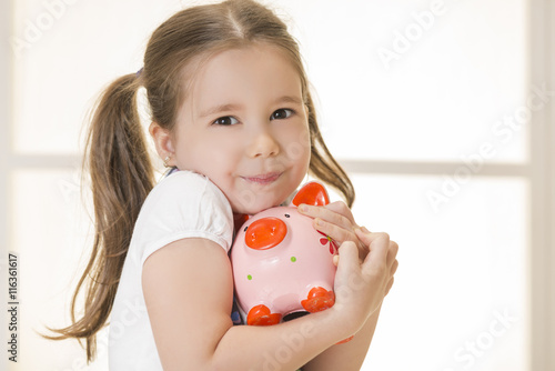 Close up portrait of happy young little girl snuggling pink piggy bank. Education, school and money saving concept. Junior Savings Account concept