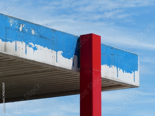 Roter Pfeiler mit heruntergekommenem blauen Dach der ehemaligen Tankstelle vor blauem Himmel im Sonnenschein im Hafenviertel oder Hansaviertel am Hansaring in Münster in Westfalen im Münsterland photo