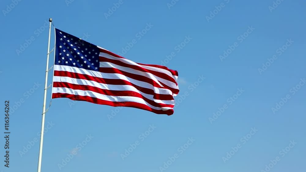 United States flag on a pole waves in the breeze against a blue sky. United States flag on a pole waves in the breeze against a blue sky.