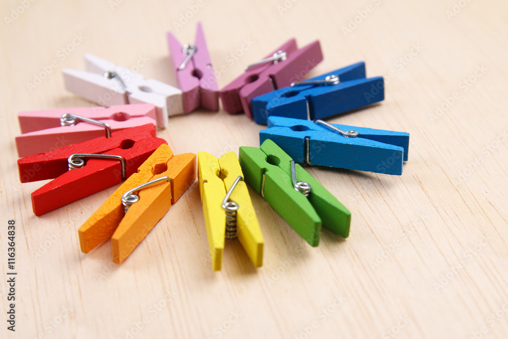 Colorful clothes pegs arranged in a circle on wooden surface Colorful clothes pegs arranged in a circle on wooden surface