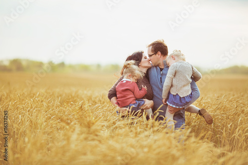 Mother and father holds on a hands their little children and kiss each other on a field