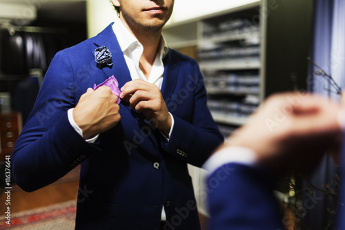 Midsection of male customer adjusting handkerchief on suit at clothing store