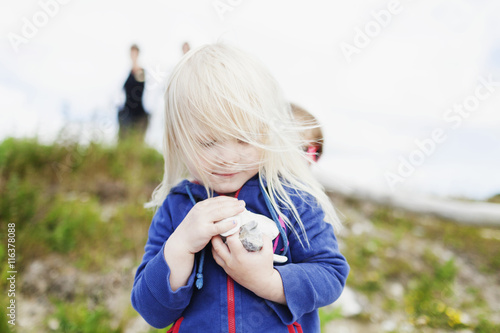 Girl holding pebbles on grassy field against barn photo