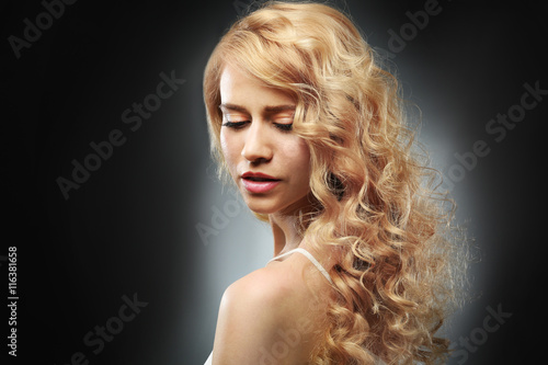 Portrait of young woman with blonde hair on dark background