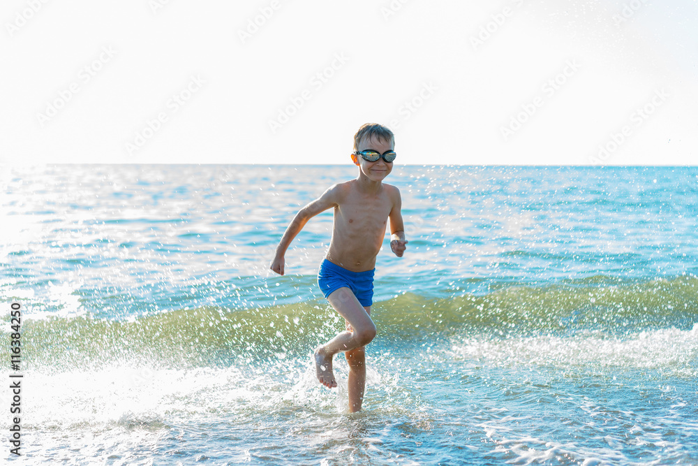 Happy small boy running with splash on the sea.