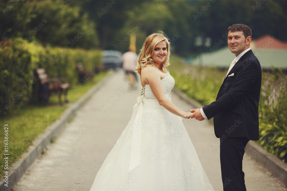 A wedding couple holds their hands together while walking along A wedding couple holds their hands together while walking along