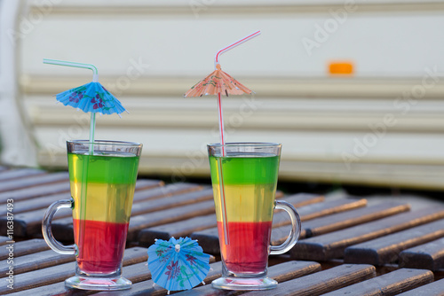 Two glasses with colorful cocktails and straws on a wooden lounger on the background Autocamper photo