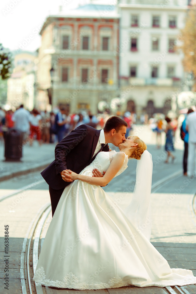 Groom bends bride over kissing her on a city square