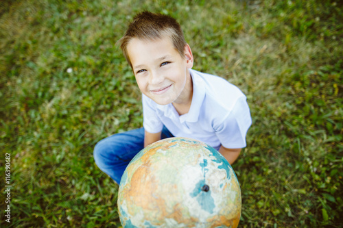 teenager boy holding a globe in his hand sitting on the grass , outdoors