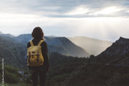 Hipster girl with backpack enjoying sunset on peak foggy mountain. Tourist traveler on background valley landscape view mockup. Hiker looking sunlight in trip Northern Spain Picos de Europa mock up