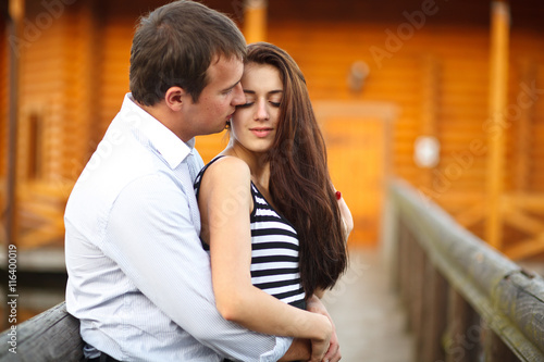 Boy kisses a tender brunette on the wooden bridge
