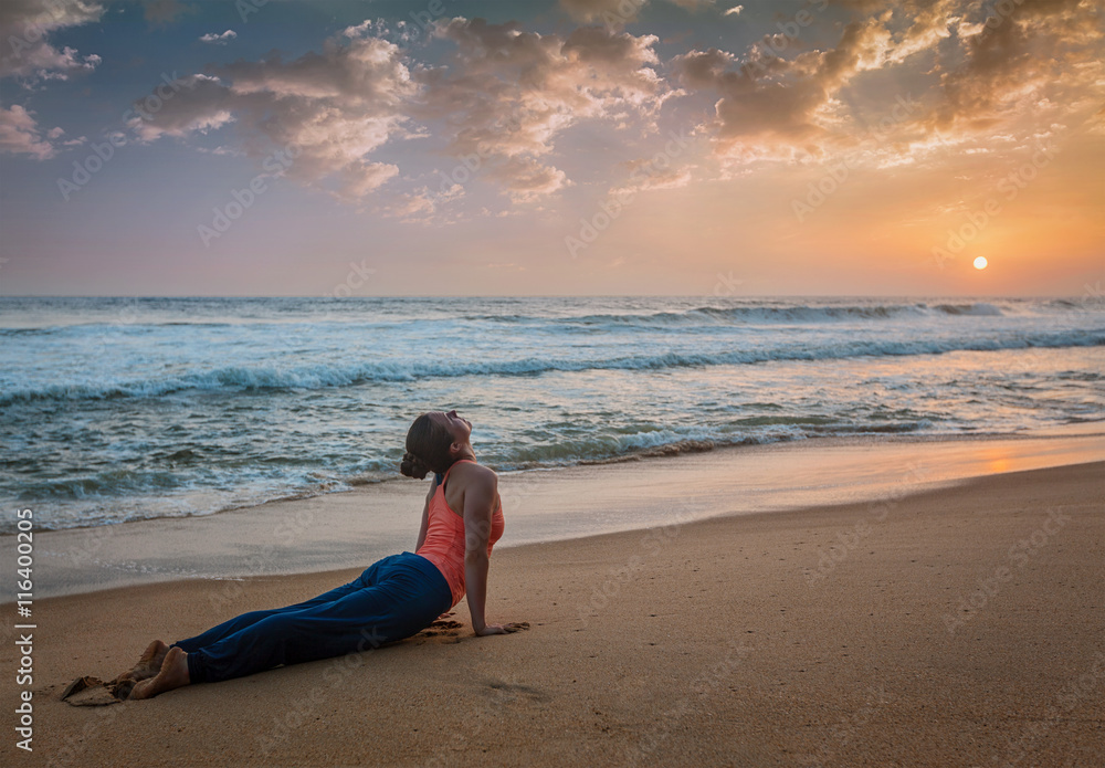 Woman practices yoga asana Urdhva Mukha Svanasana at the beach