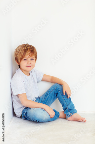 handsome young boy, kid sitting near the white wall