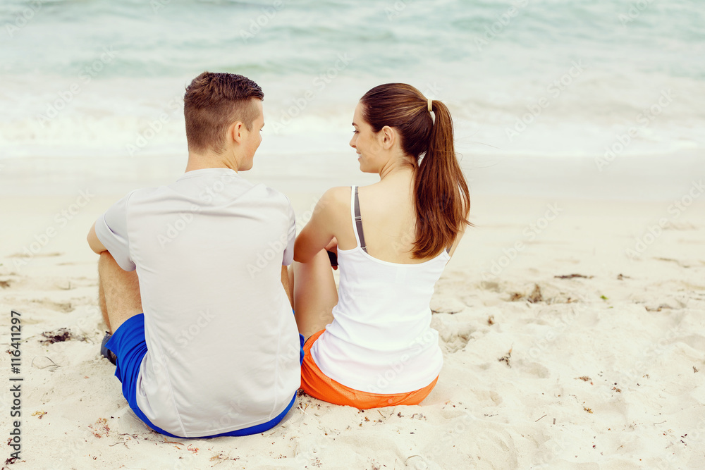 Fototapeta premium Young couple looking at each other while sitting on beach