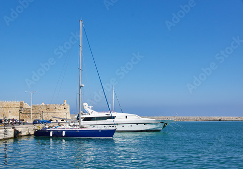Two yachts at the pier In the Bay of Heraklion on the background of the walls of the old castle