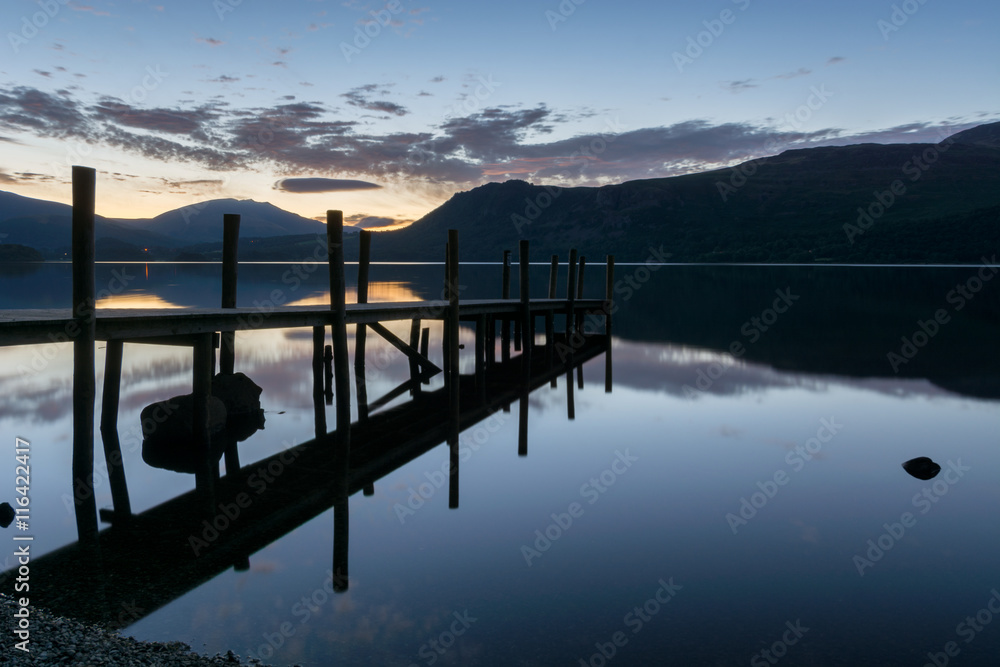 Beautiful dawn blue hour reflections at Derwentwater Lake with silhouetted jetty.