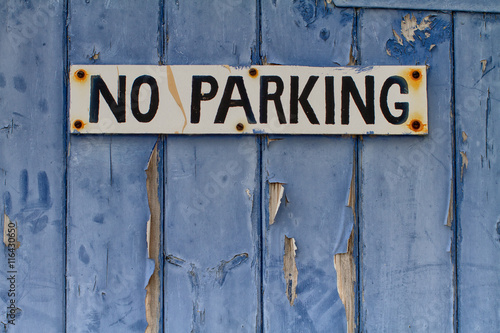 No Parking sign on an old blue wooden door with peeling paint