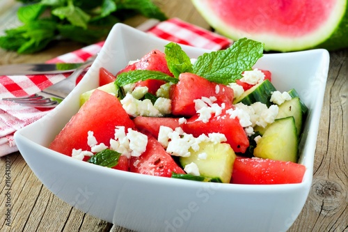 Delicious watermelon, cucumber and feta cheese salad in square bowl on wood background
