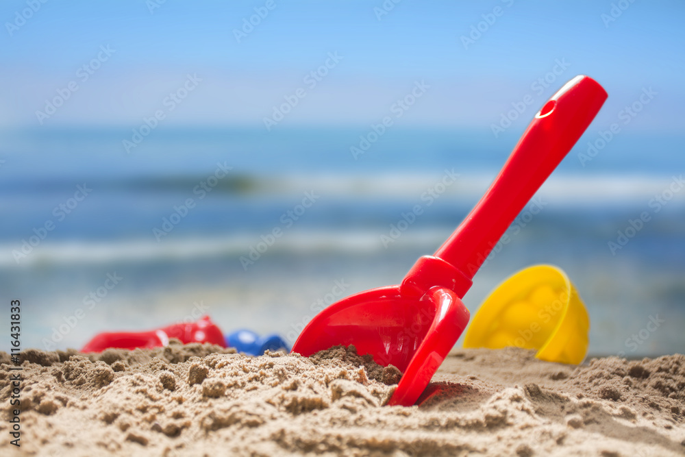red toy shovel and plastic molds in the sand at the beach red toy shovel and plastic molds in the sand at the beach