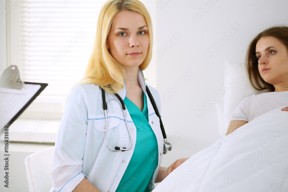 Young beautiful female doctor sitting near the bed of her patient in hospital. Young beautiful female doctor sitting near the bed of her patient in hospital.