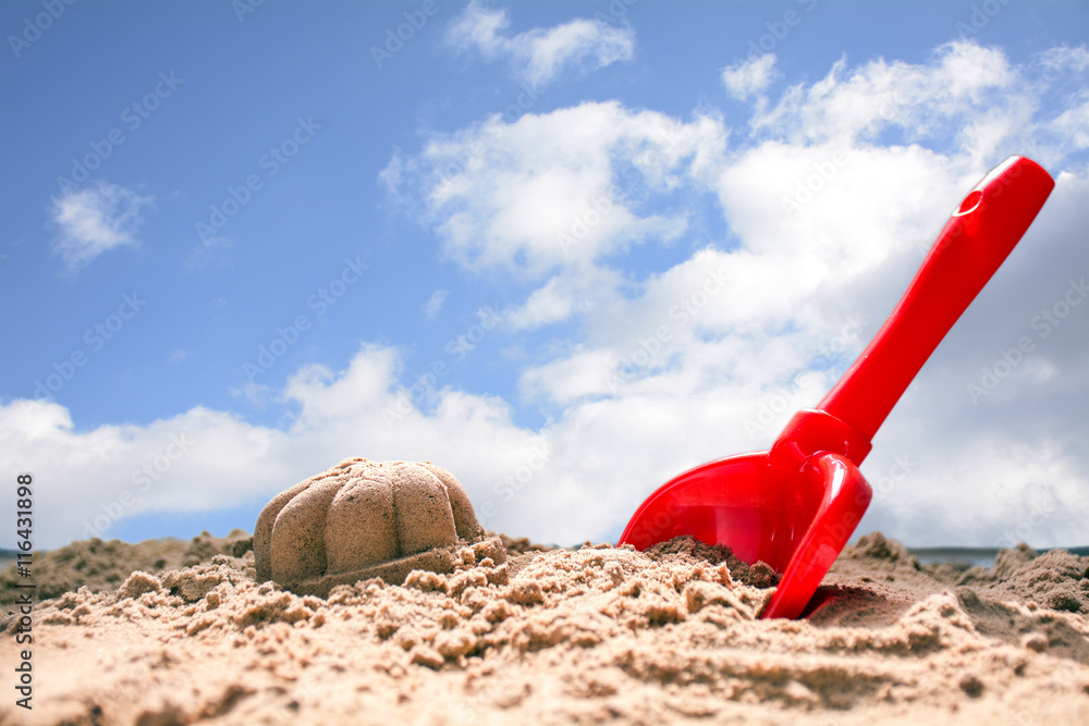red toy shovel and molded sand on the beach against the blue sky red toy shovel and molded sand on the beach against the blue sky
